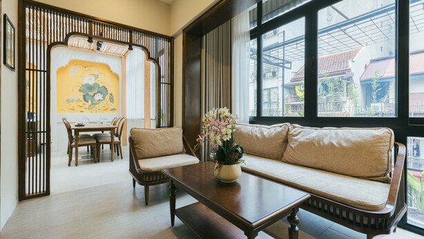 A traditional-style living room with a sofa, a dining table with chairs, and a large window offering a view of buildings outside. - Lily Hidden Homestay – Boutique Stay in the Heart of Hanoi Old Quarter (Hà Nội)