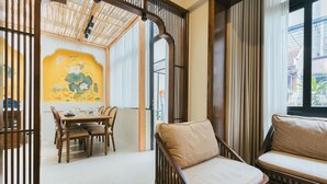 A dining area with a wooden table and chairs, a cushioned sofa, and a decorative wall with a lotus painting. - Lily Hidden Homestay – Boutique Stay in the Heart of Hanoi Old Quarter (Hà Nội)