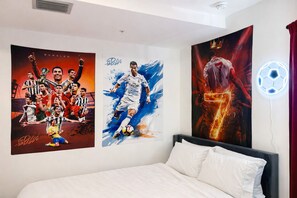 Ein Schlafzimmer mit einem Bett, einer Wandleuchte und drei Sportplakaten.