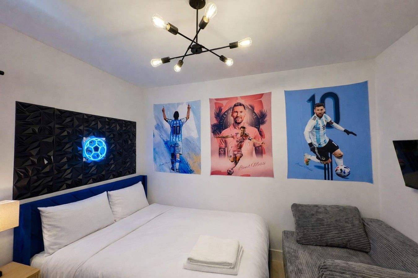 Een hotelkamer met een bed, een bureau, een stoel, een wandlamp en sportgerelateerde kunstwerken.
