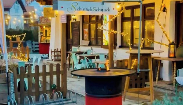 An outdoor seating area with tables and chairs, a sign reading 'SchindlerSchnack,' and a decorative fence. - Charming country hotel, 13 rooms, sauna, whirlpool, pet-friendly & central (Flintsbach am Inn)