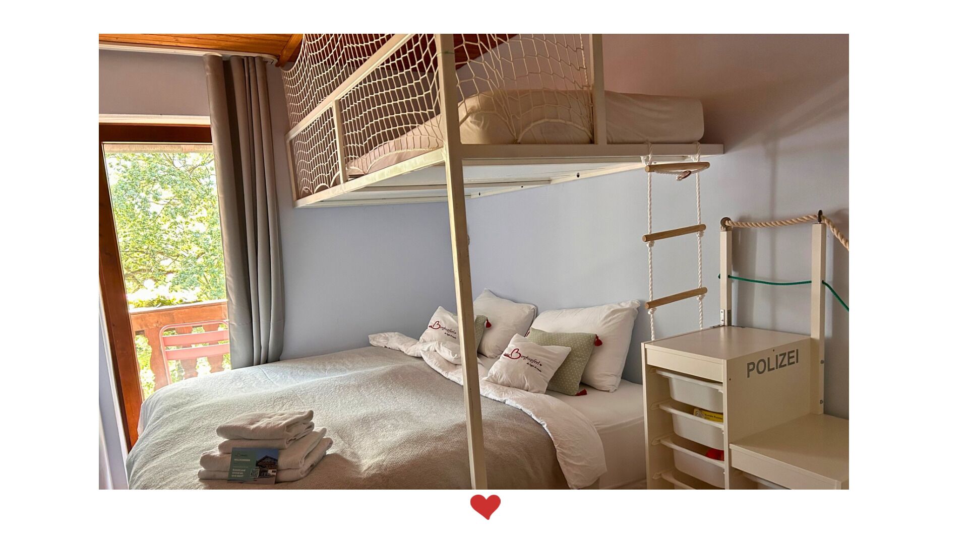 A bunk bed room with a wooden ladder, a small desk, and a window with curtains.