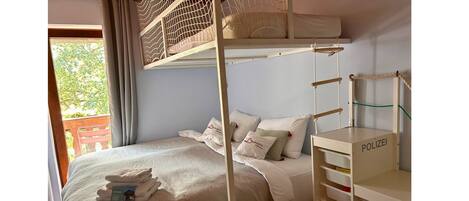 A bunk bed room with a wooden ladder, a small desk, and a window with curtains.