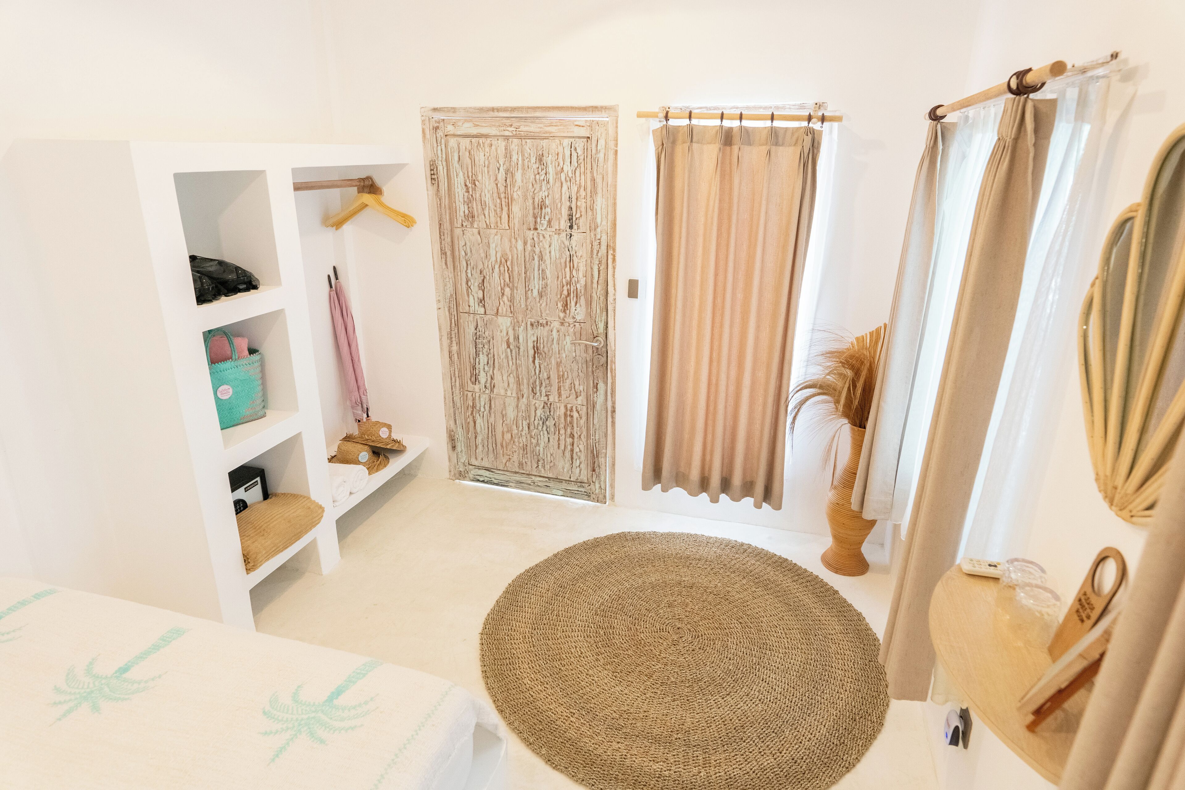A room with a white wardrobe, a round woven rug, and a wooden door.