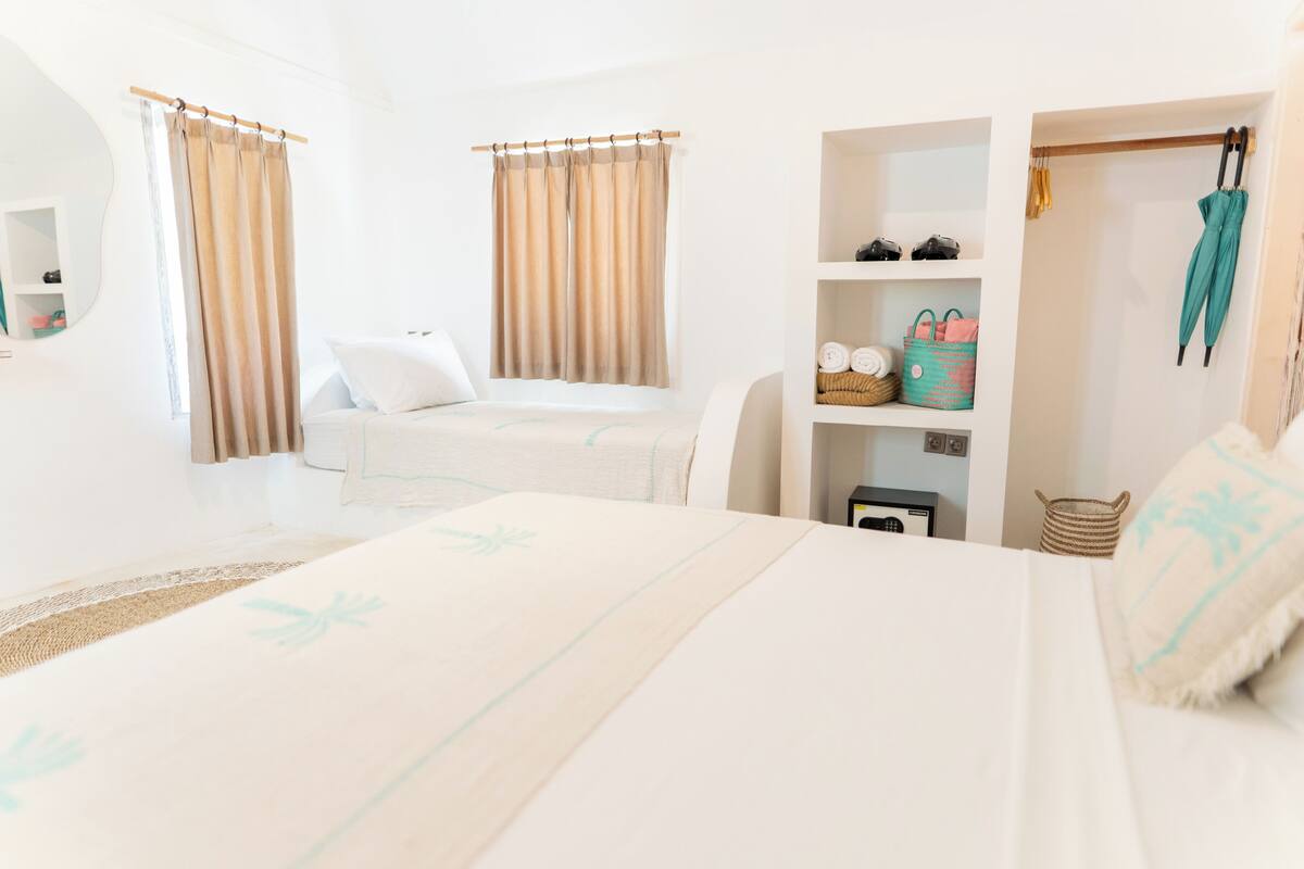 A hotel room with a bed, a wardrobe, a shelf with bags, and a mirror.