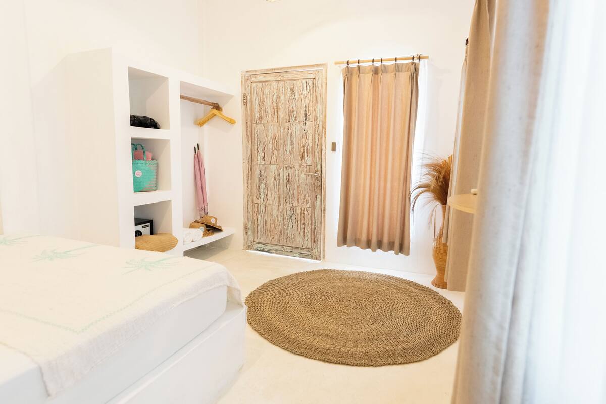 A bedroom with a bed, a wardrobe, a shelf with bags, and a round rug.