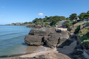 A coastal landscape with rocky cliffs, a beach, and a staircase leading up to a building. - Apartment for 4  with sea view and balcony (Pornic)