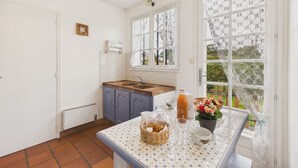 Een keuken met een raam, een spoelbak, kastjes en een tafel met een mand en bloemen.
