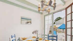 Een eetgedeelte met een tafel voor vier personen, witte stoelen en uitzicht op de omgeving door een glazen deur.