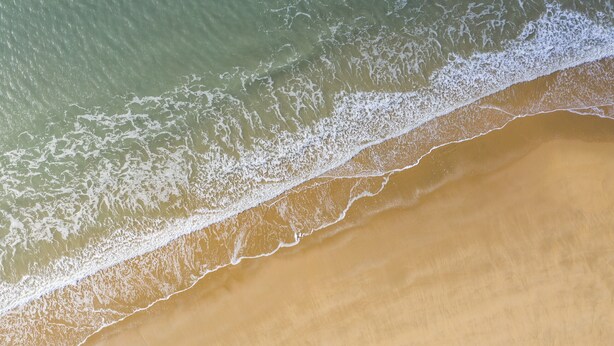 Een luchtbeeld van een strand met een duidelijke grens tussen de oceaan en het zandstrand.