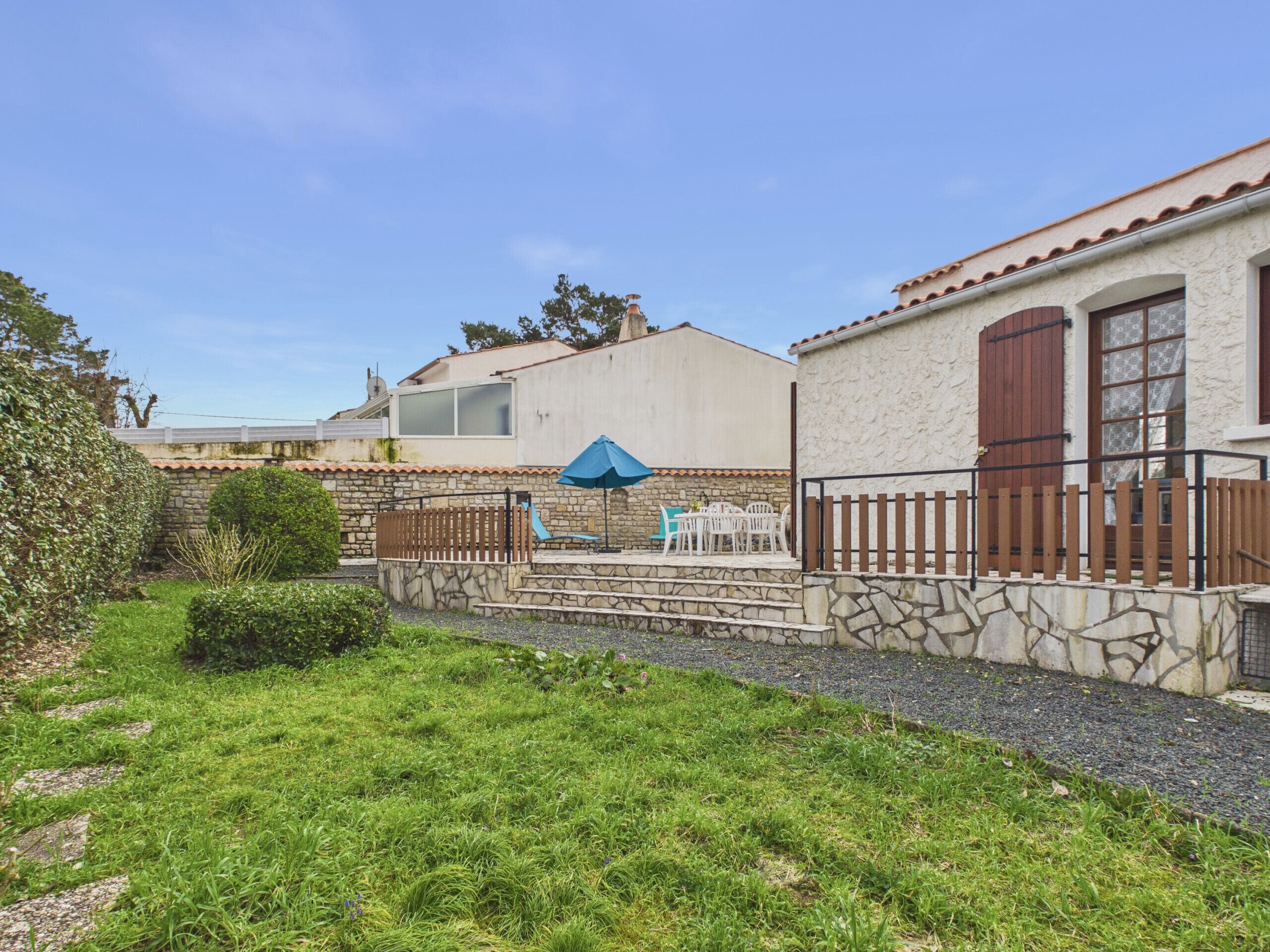 Un immobile residenziale con una scala in pietra che conduce a un patio, un piccolo giardino e un edificio con tetto in tegole e persiane in legno.