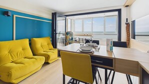A modern room with a large window, a dining table, yellow chairs, and a yellow sofa. - Breathtaking ocean view, stay for 2 (Saint-Hilaire-de-Riez)