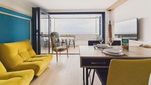 A modern room with a yellow sofa, a dining table set with plates and glasses, a patterned chair, and a TV on the wall. - Breathtaking ocean view, stay for 2 (Saint-Hilaire-de-Riez)