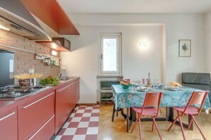 Eine kleine Küche mit roter Arbeitsplatte, einem Esstisch für vier Personen und einem Fenster über der Spüle.