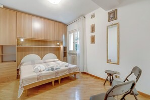 A bedroom with a bed, wooden wardrobe, bedside table, mirror, and a chair. - Clara House - Park & Garden Private (Gardone Riviera)