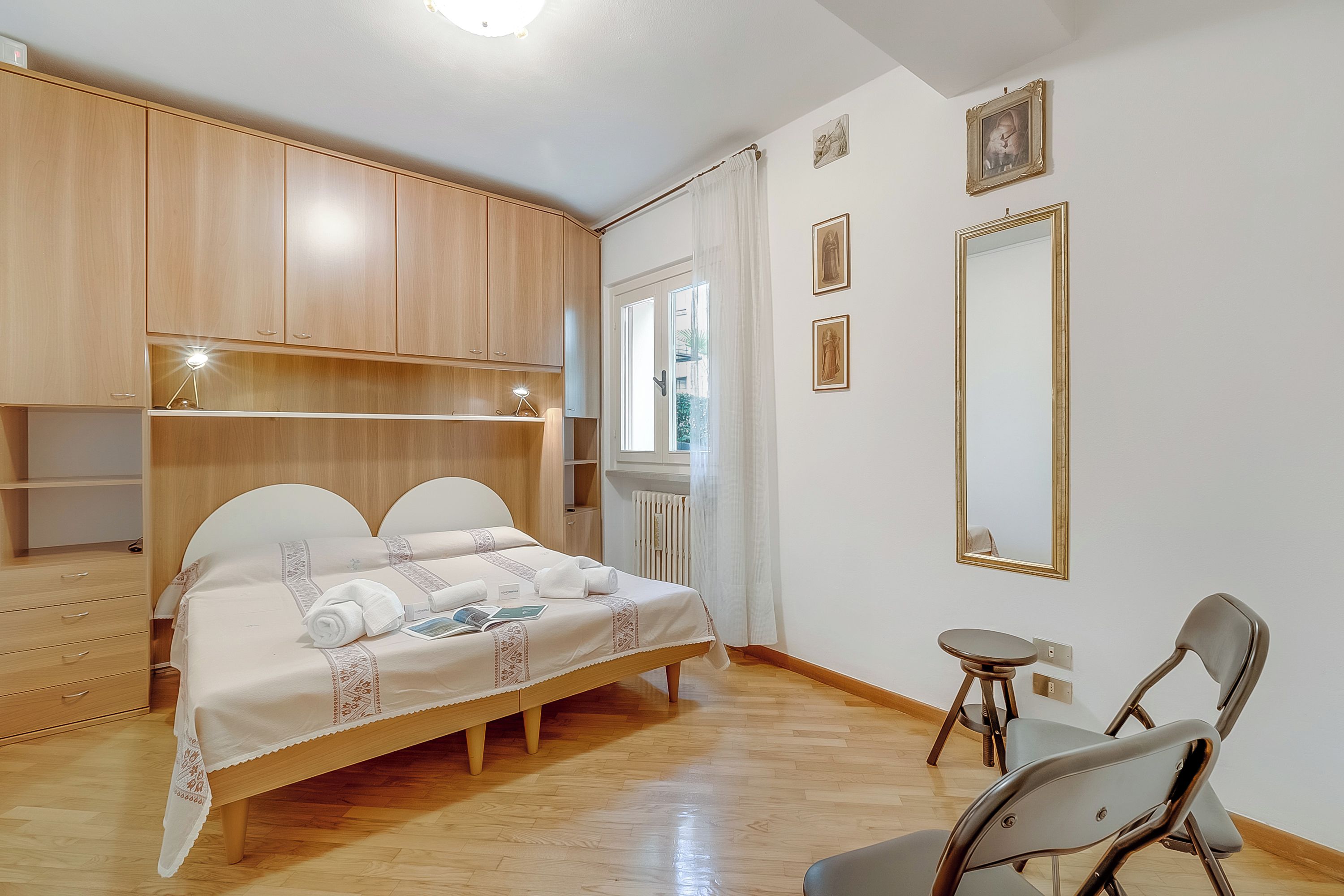 Un dormitorio con cama, armario de madera, mesita de noche, espejo y una silla.