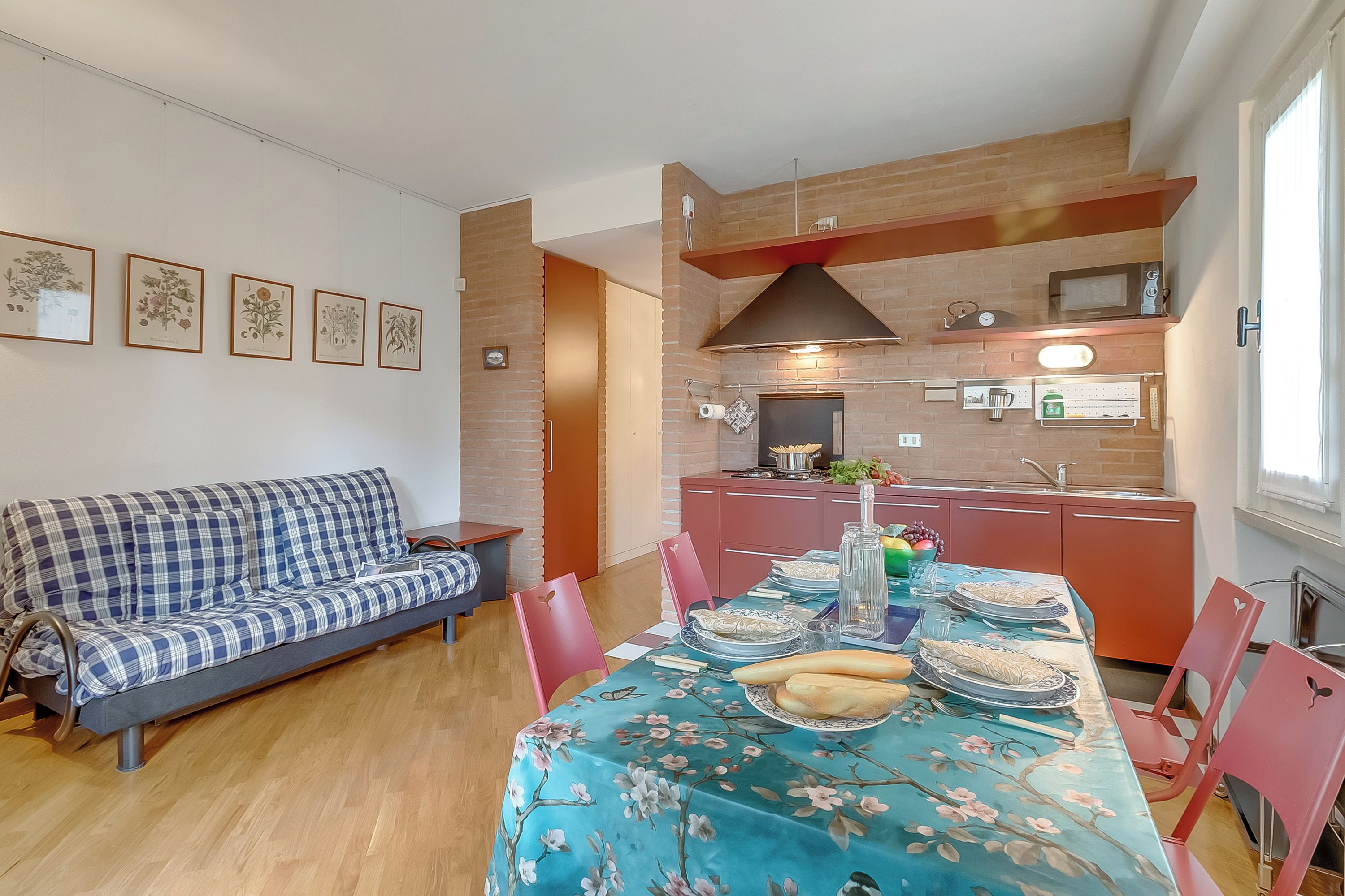A dining area with a table set for two, a sofa, and a kitchen in the background.