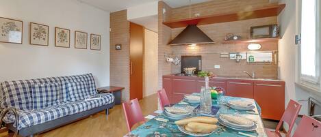 Un comedor con una mesa preparada para dos personas, un sofá y una cocina al fondo.