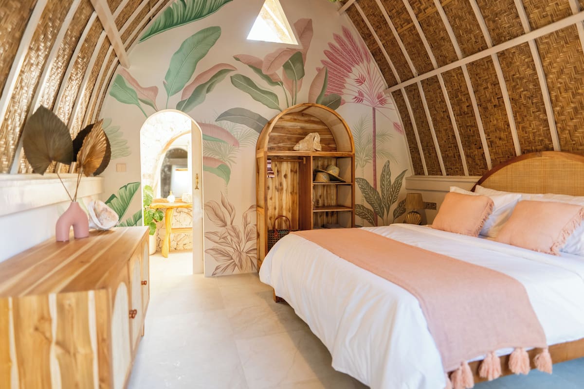 A room with a bed, wooden furniture, a mirror, and a wall with a leaf pattern.