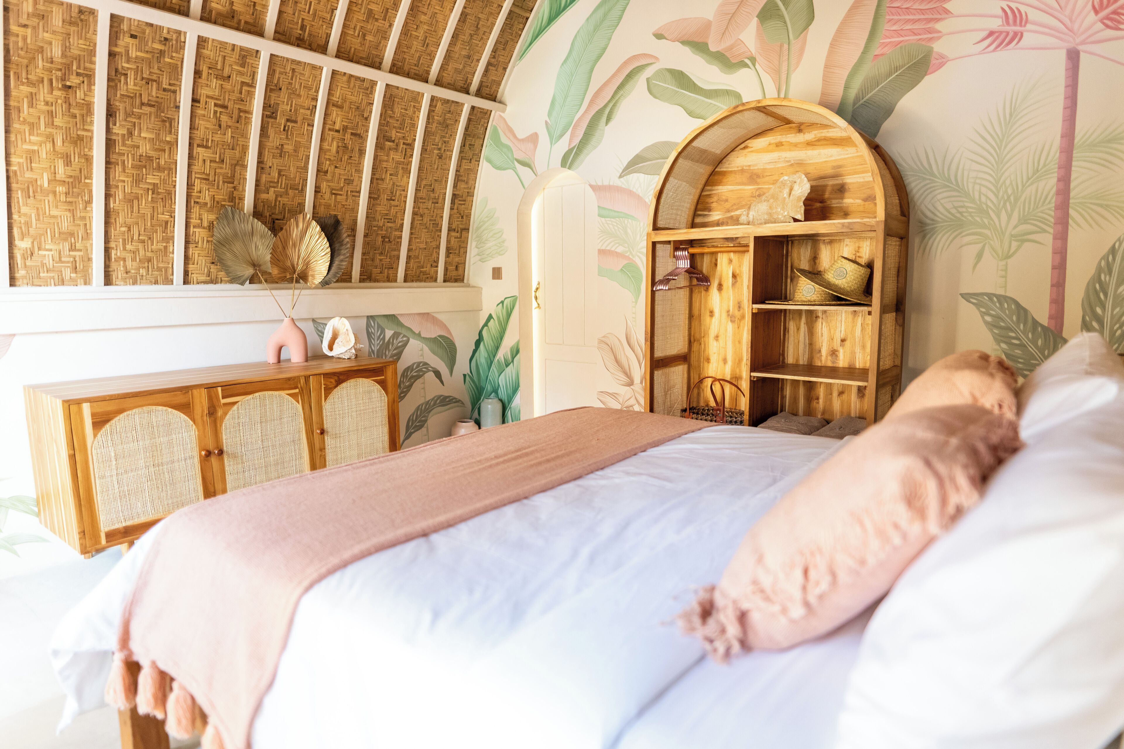 Une chambre à coucher avec un lit, une armoire en bois dotée d’une étagère et un mur orné d’un motif de feuilles.