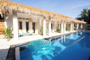 A poolside area with a thatched roof, a clear blue pool, and a lounge chair. - Isla de Agua (Gili Air)