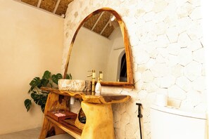 Un baño con pared de piedra, tocador de madera con lavamanos, espejo y planta.