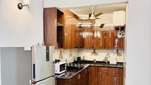 Eine kleine Küche mit Kühlschrank, Holzschränken, einer Mikrowelle und einer gefliesten Spritzschutzwand.