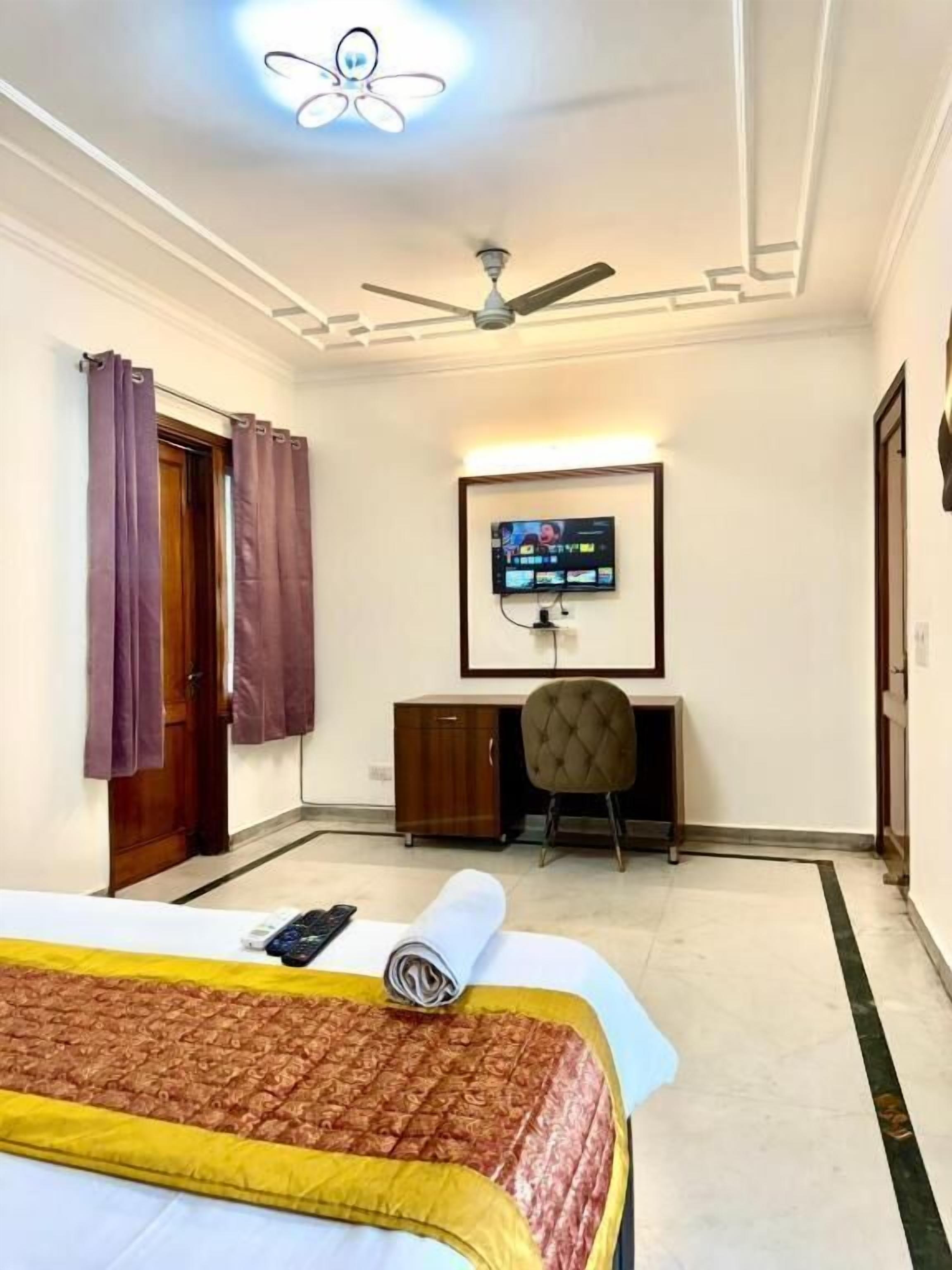 A hotel room with a bed, a desk, a chair, a ceiling fan, and a TV mounted on the wall.