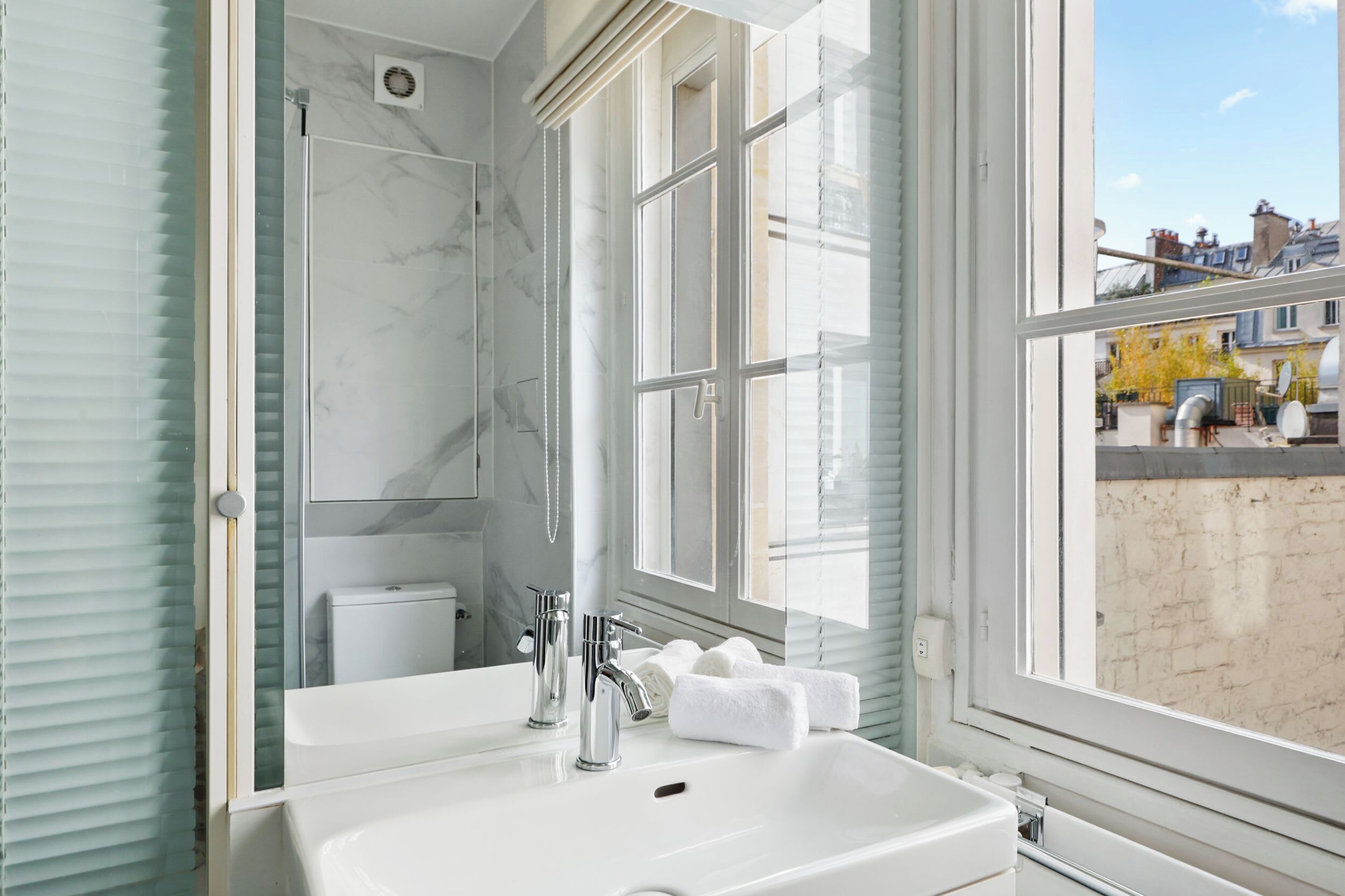 A bathroom with a large window, a shower, and a sink with two faucets.