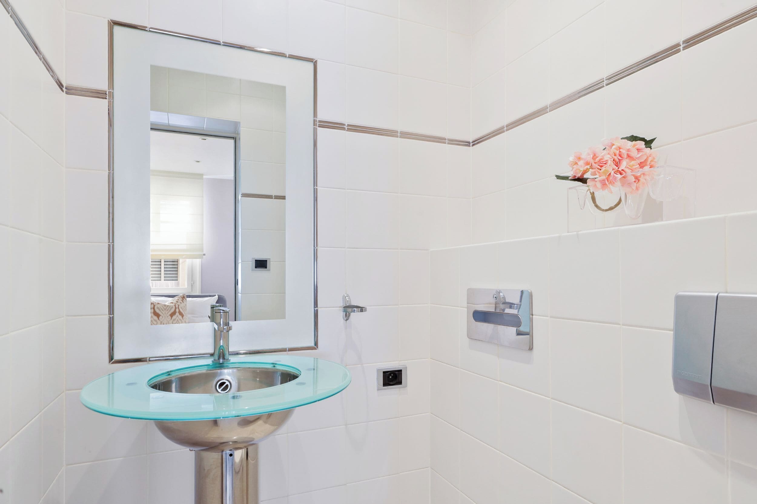A modern bathroom with a glass sink, a large mirror, and a wall-mounted dispenser.