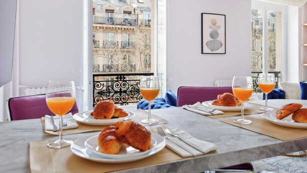 A breakfast table with croissants and orange juice, set against a city view. - Chic 2BR Near Le Louvre & Palais Royal (Paris)
