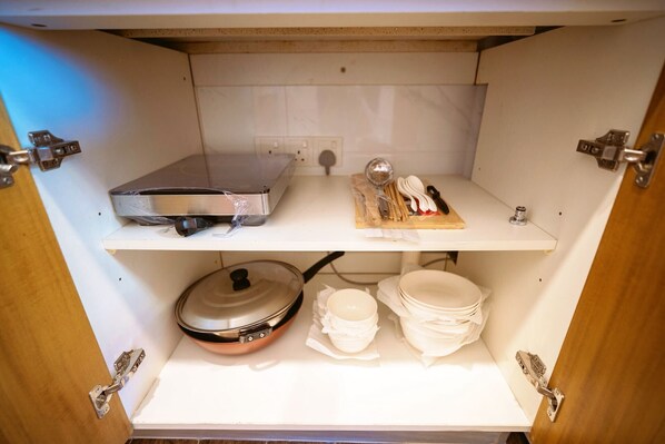 A kitchen cabinet with a microwave, a cutting board with utensils, and stacked bowls.