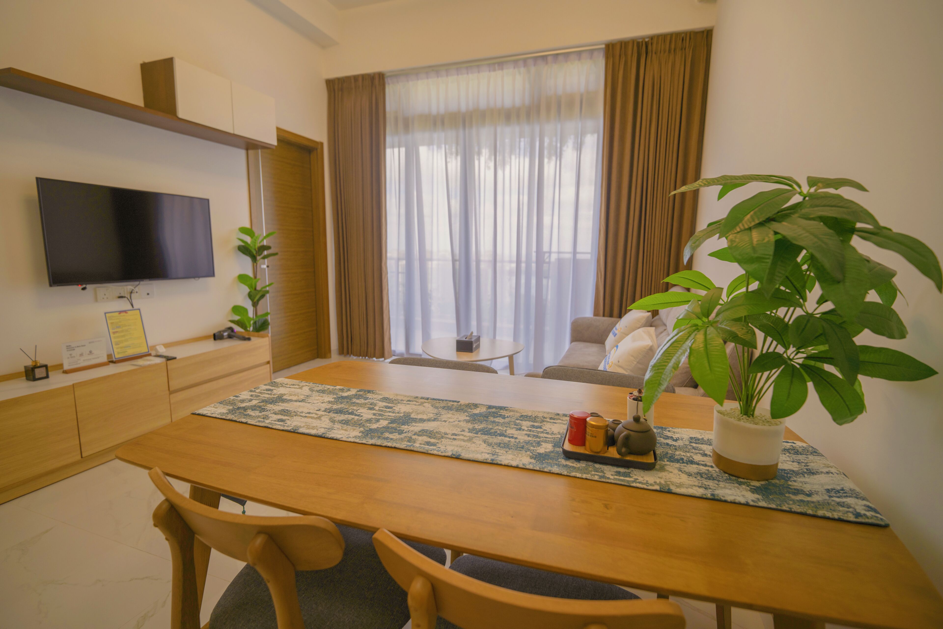 Una sala moderna con una televisión de pantalla plana, una mesa de comedor con sillas, un sofá, una mesa de centro y dos plantas en macetas.