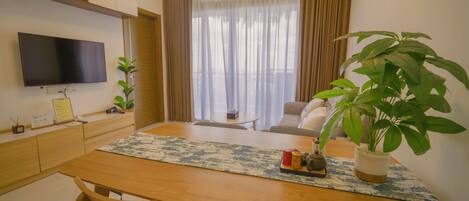 Una sala moderna con una televisión de pantalla plana, una mesa de comedor con sillas, un sofá, una mesa de centro y dos plantas en macetas.