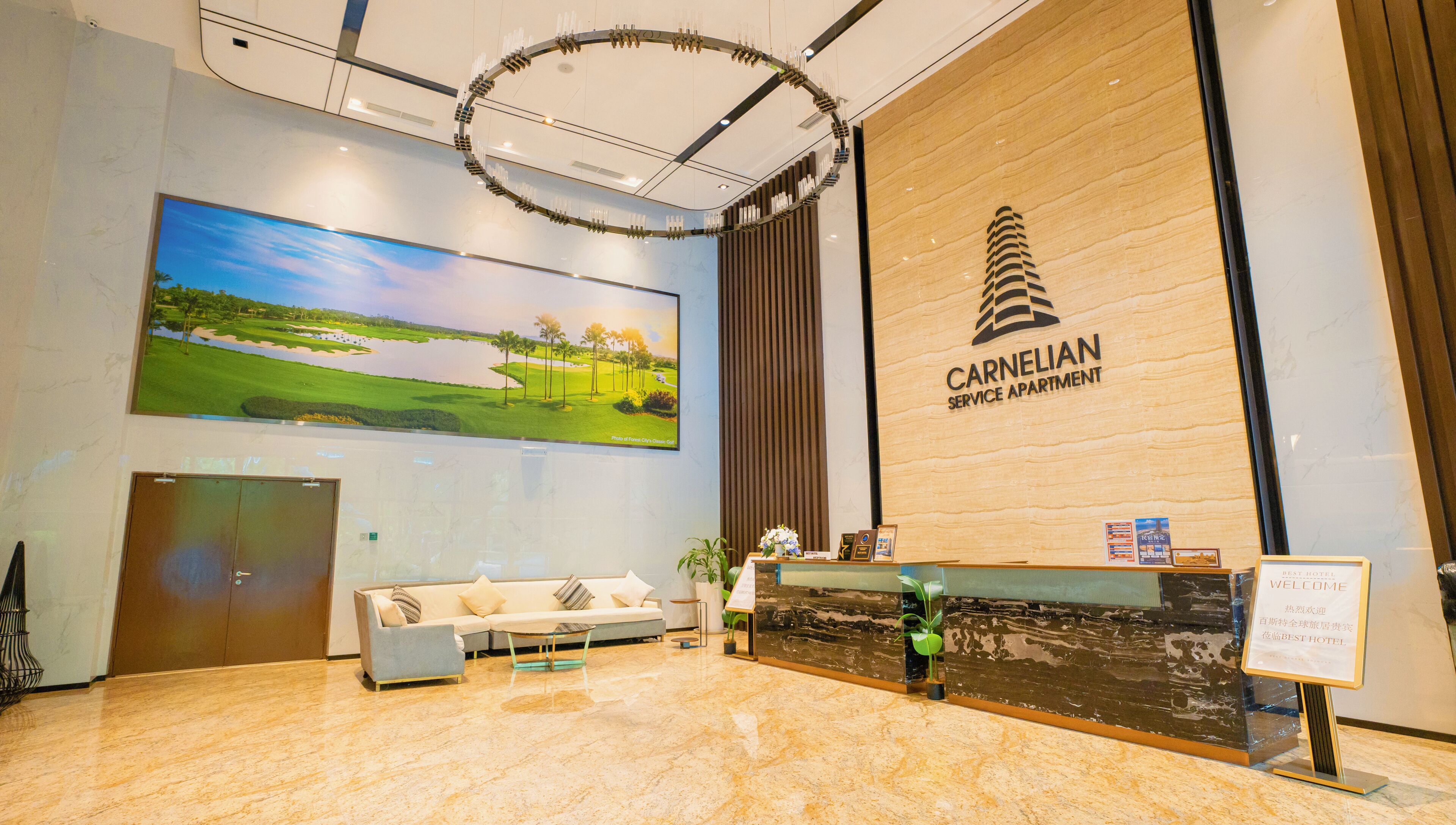 A reception area with a large screen displaying a golf course, a reception desk, a sofa, and a sign for the Carnelian Service Apartment.