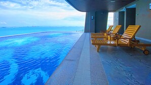 Une piscine à débordement offrant une vue sur l’océan, des chaises longues en bois et un espace abrité.