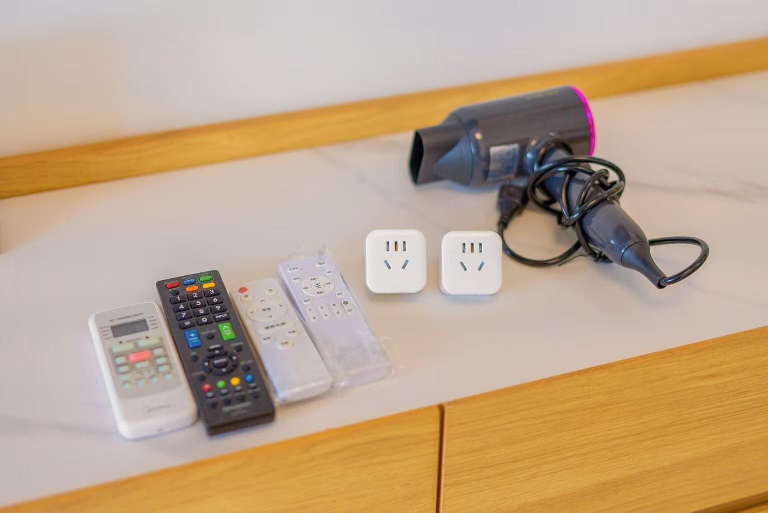 A marble-topped table with various remote controls, a hairdryer, and a power strip.