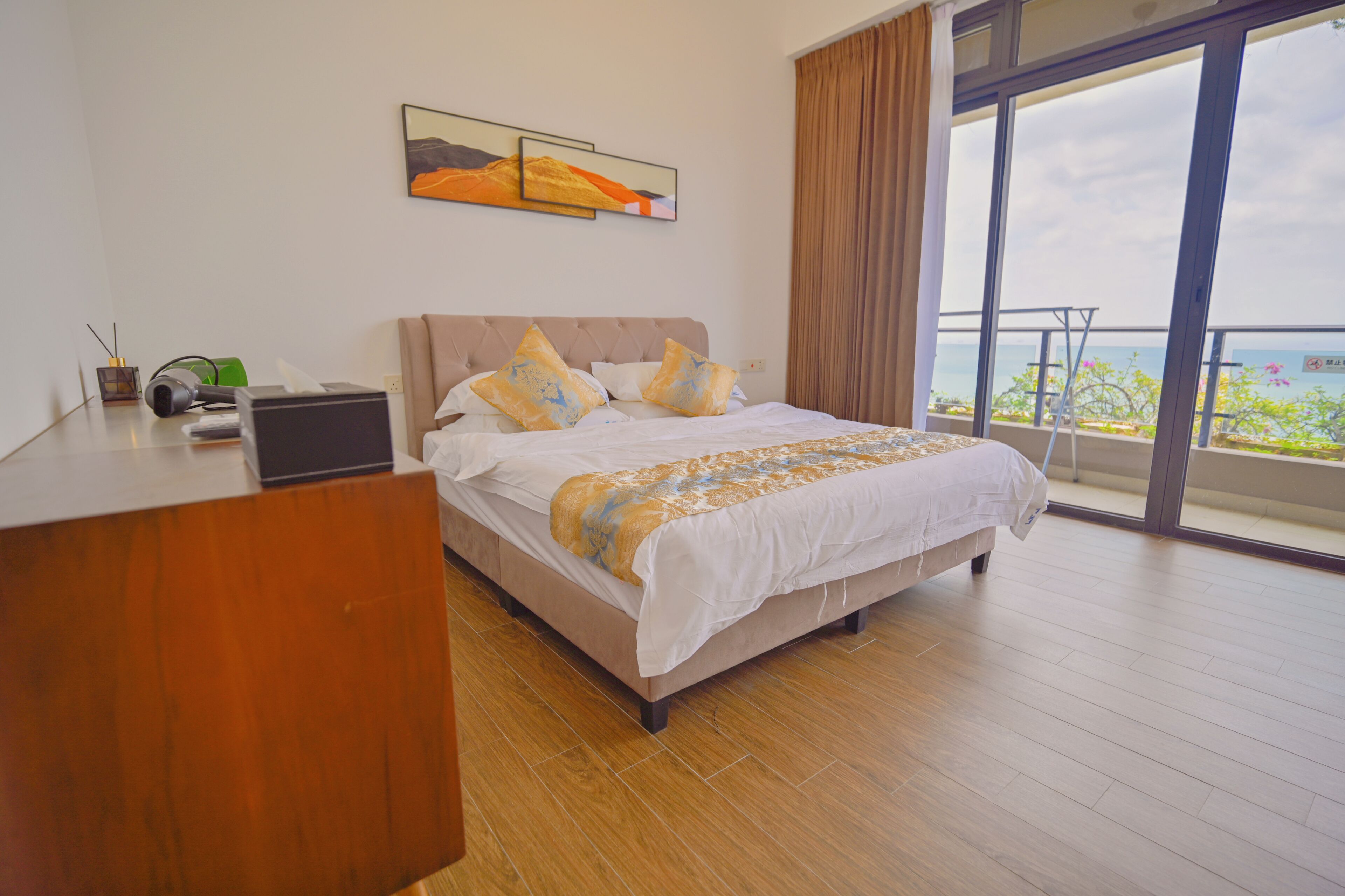 A bedroom with a bed, a desk, a laptop, and a painting on the wall.