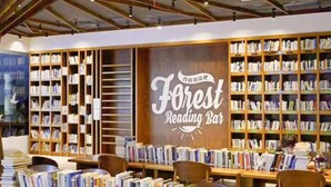 Un bar à lecture chaleureux, doté d’étagères à livres, de tables et de chaises en bois, et d’une enseigne indiquant : « Bar à lecture Forest. »