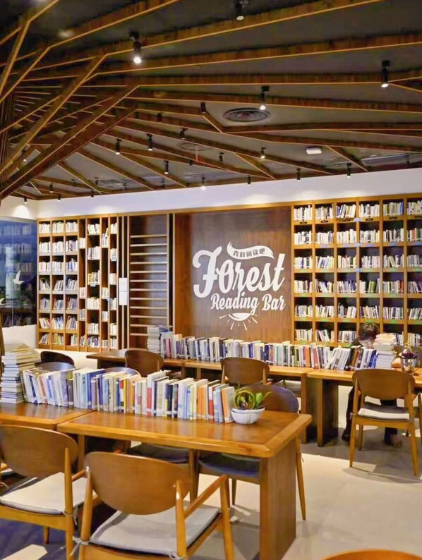 Eine gemütliche Lesebar mit Bücherregalen, Holztischen und -stühlen, und einem Schild mit der Aufschrift 'Forest Reading Bar'.