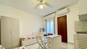 A compact room with a bed, a desk, a chair, a ceiling fan, a microwave, and a window. - Studio with balcony close to the beach (Porto Santa Margherita)