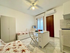 A compact room with a bed, a desk, a chair, a ceiling fan, a microwave, and a window. - Studio with balcony by the beach (Porto Santa Margherita)
