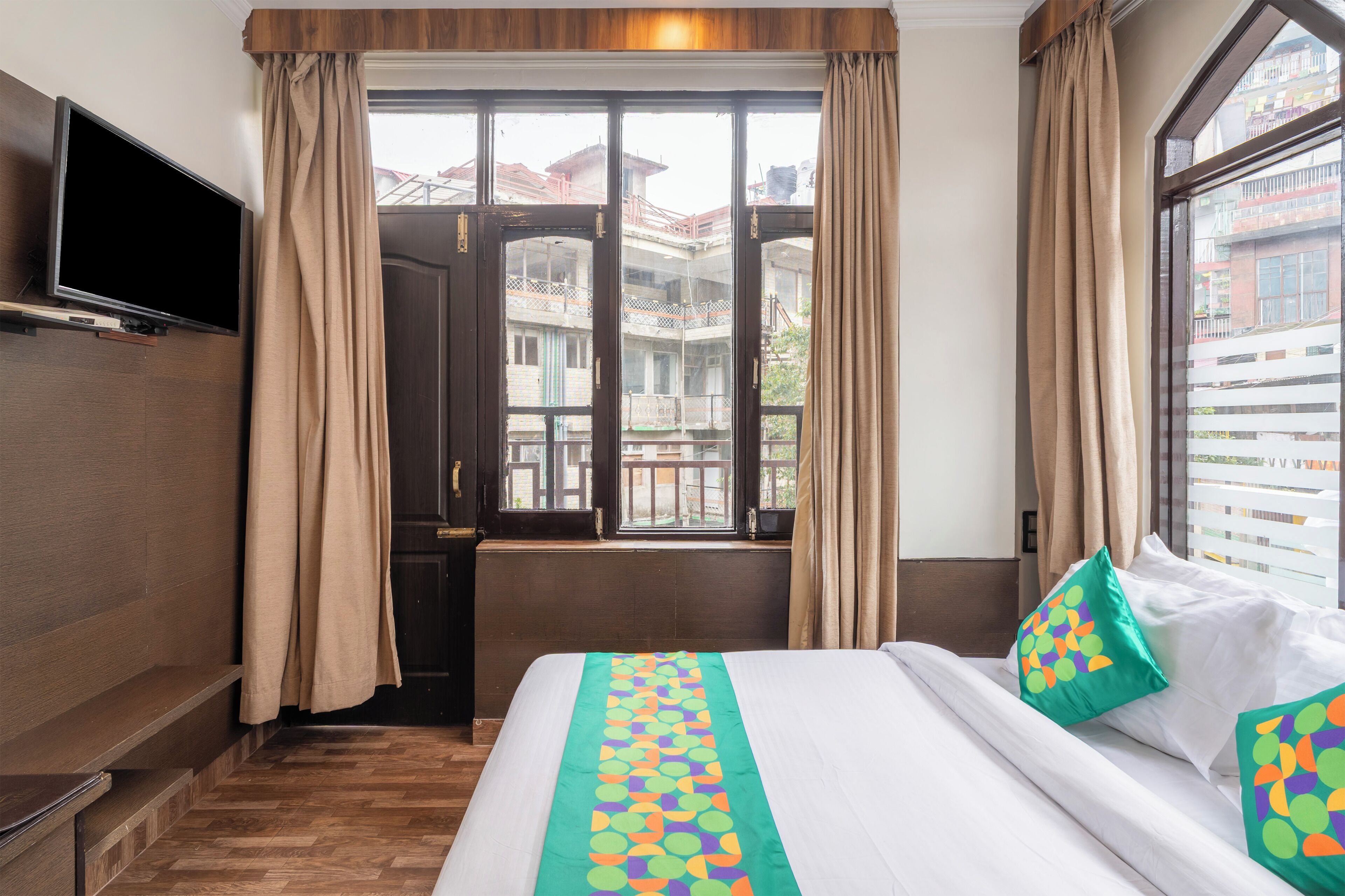 A hotel room with a bed, curtains, a television, and a window with a view of buildings.