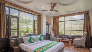 A hotel room with a large bed, a desk, a chair, and a ceiling fan. - Treebo Holiday Hill (Dharamshala)