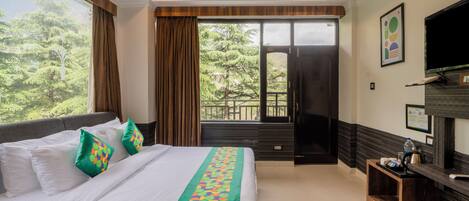 A hotel room with a large bed, a TV, a desk, and a view of trees.