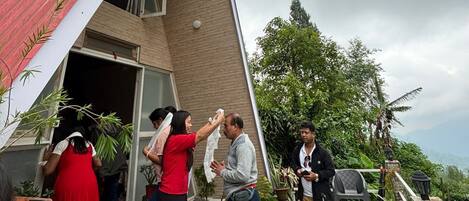 A group of people outside a building with a sloped roof, surrounded by potted plants and a scenic view.