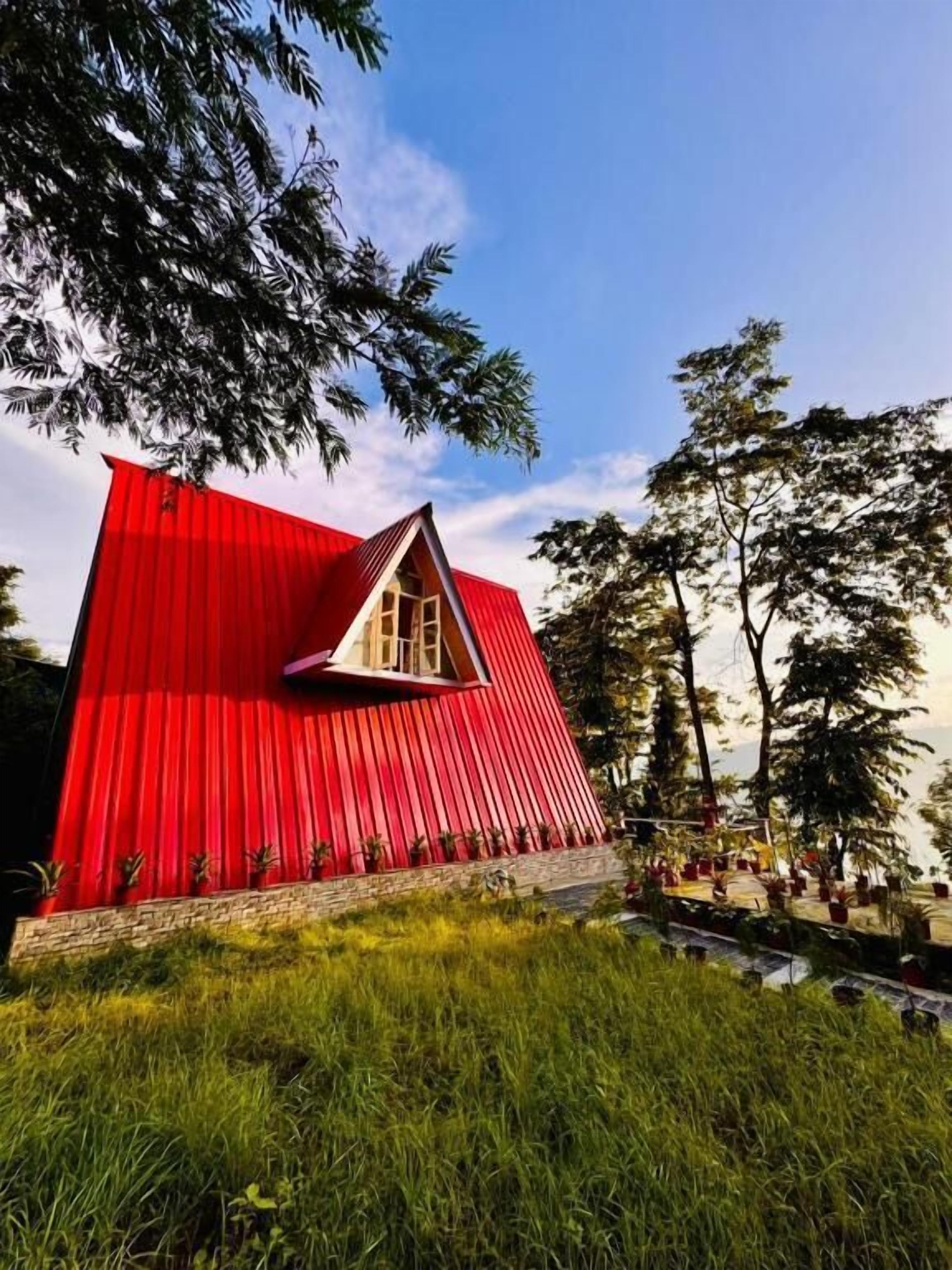 A red, triangular-shaped building with a small window and a stone base.