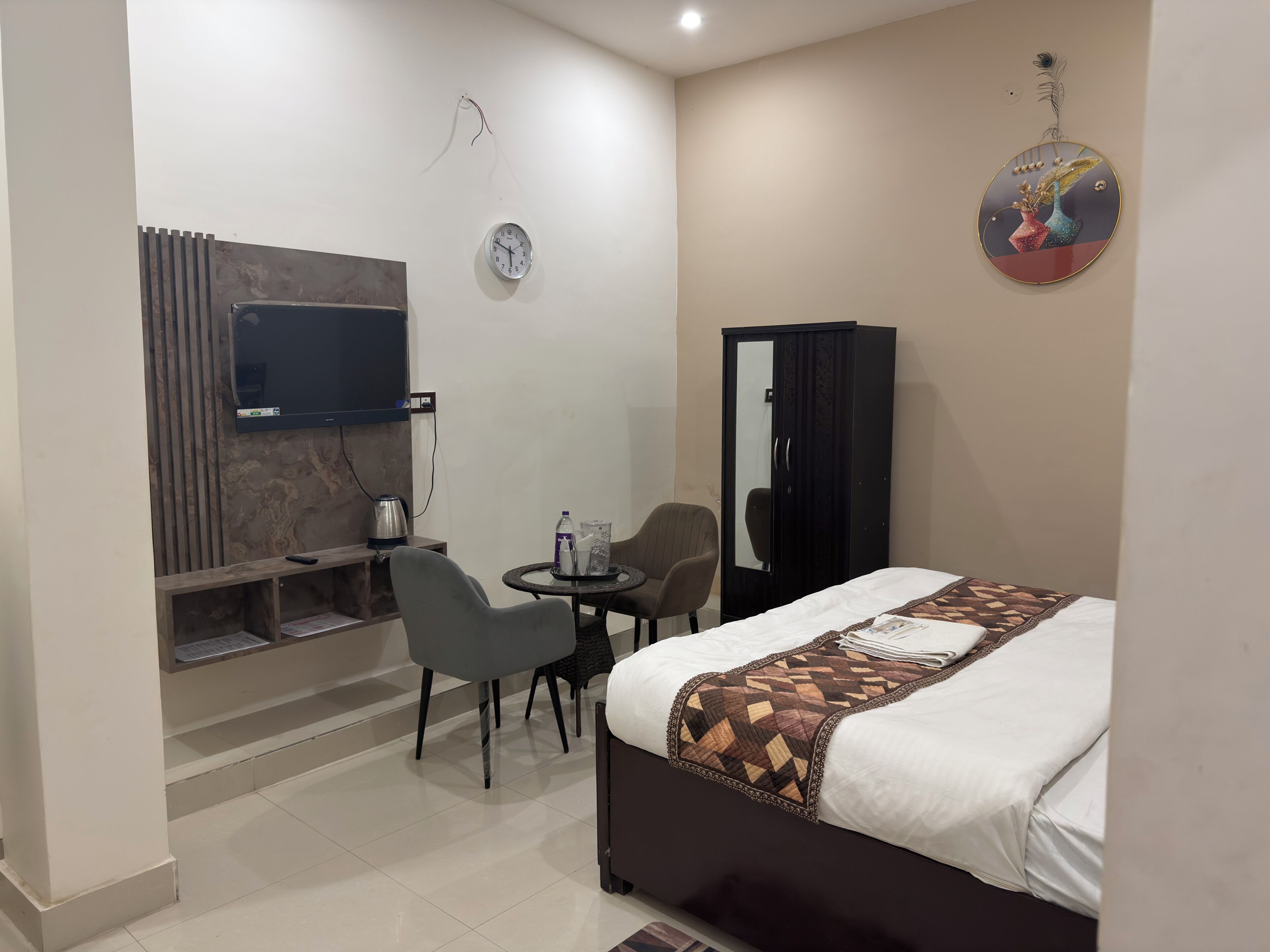 Habitación de hotel con cama, escritorio con silla, televisión, armario y reloj de pared.