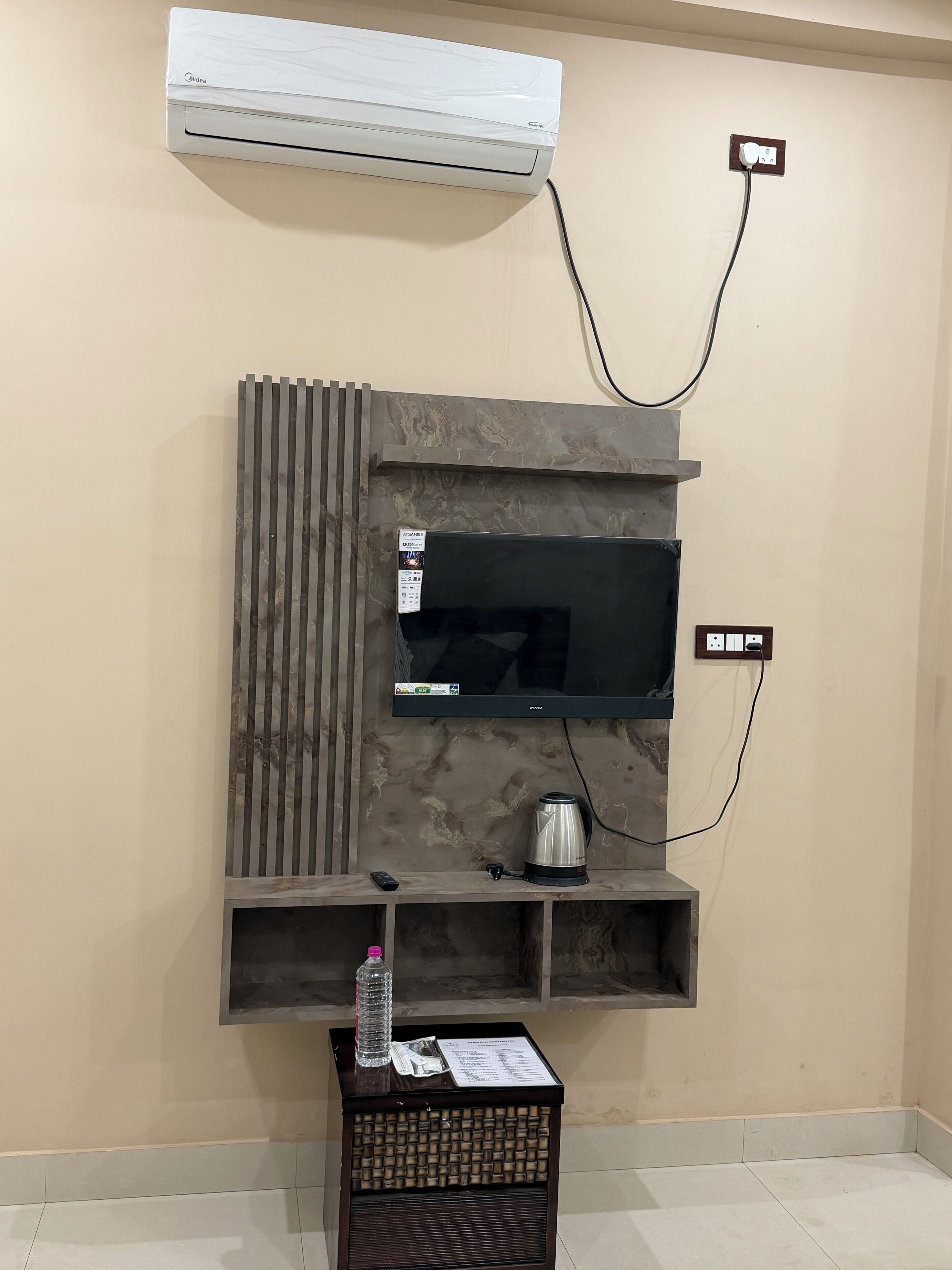 A wall-mounted entertainment unit with a flat-screen TV, a coffee maker, and a water bottle on a small table below.