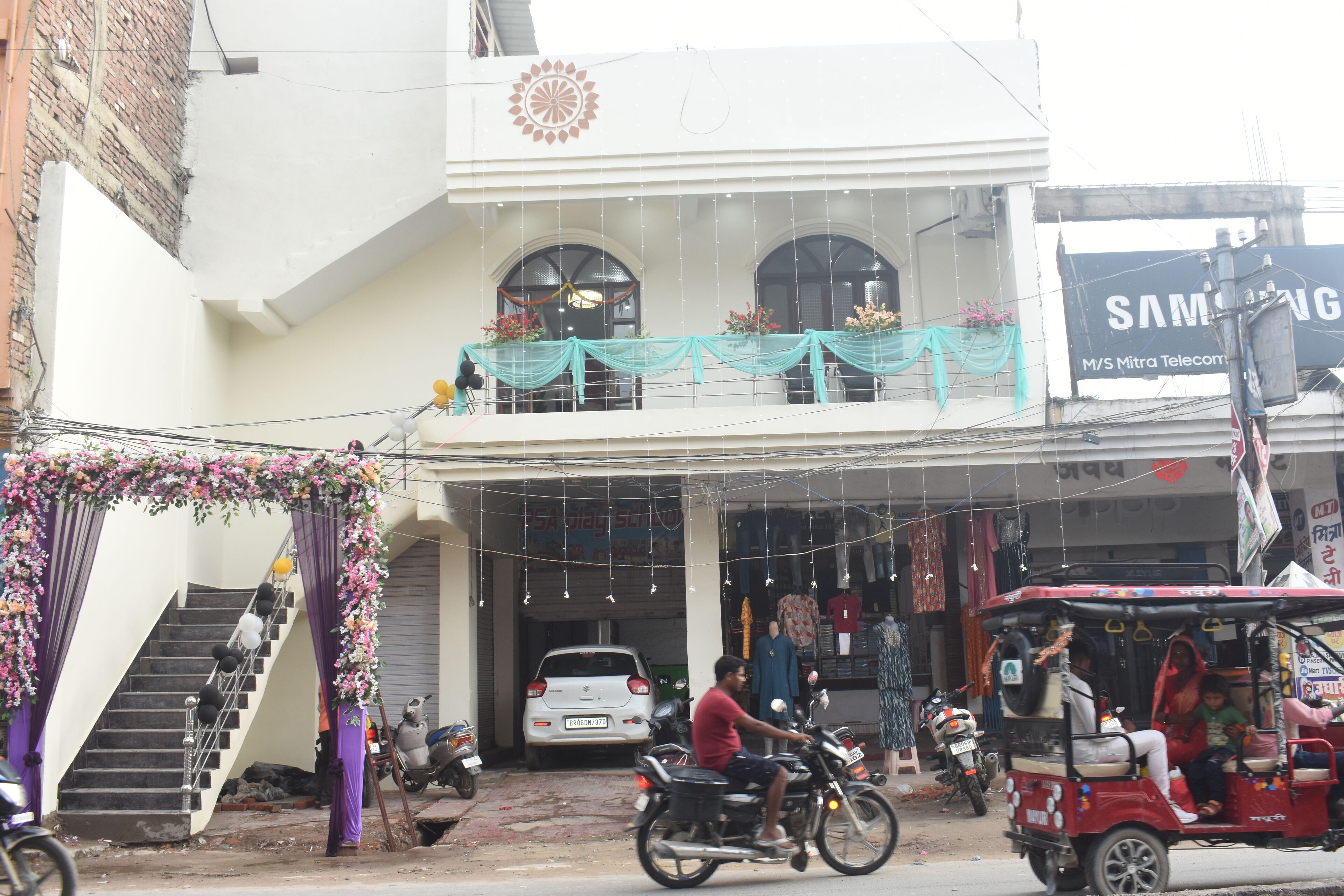 A building with a staircase, a car parked in front, and a motorcycle.